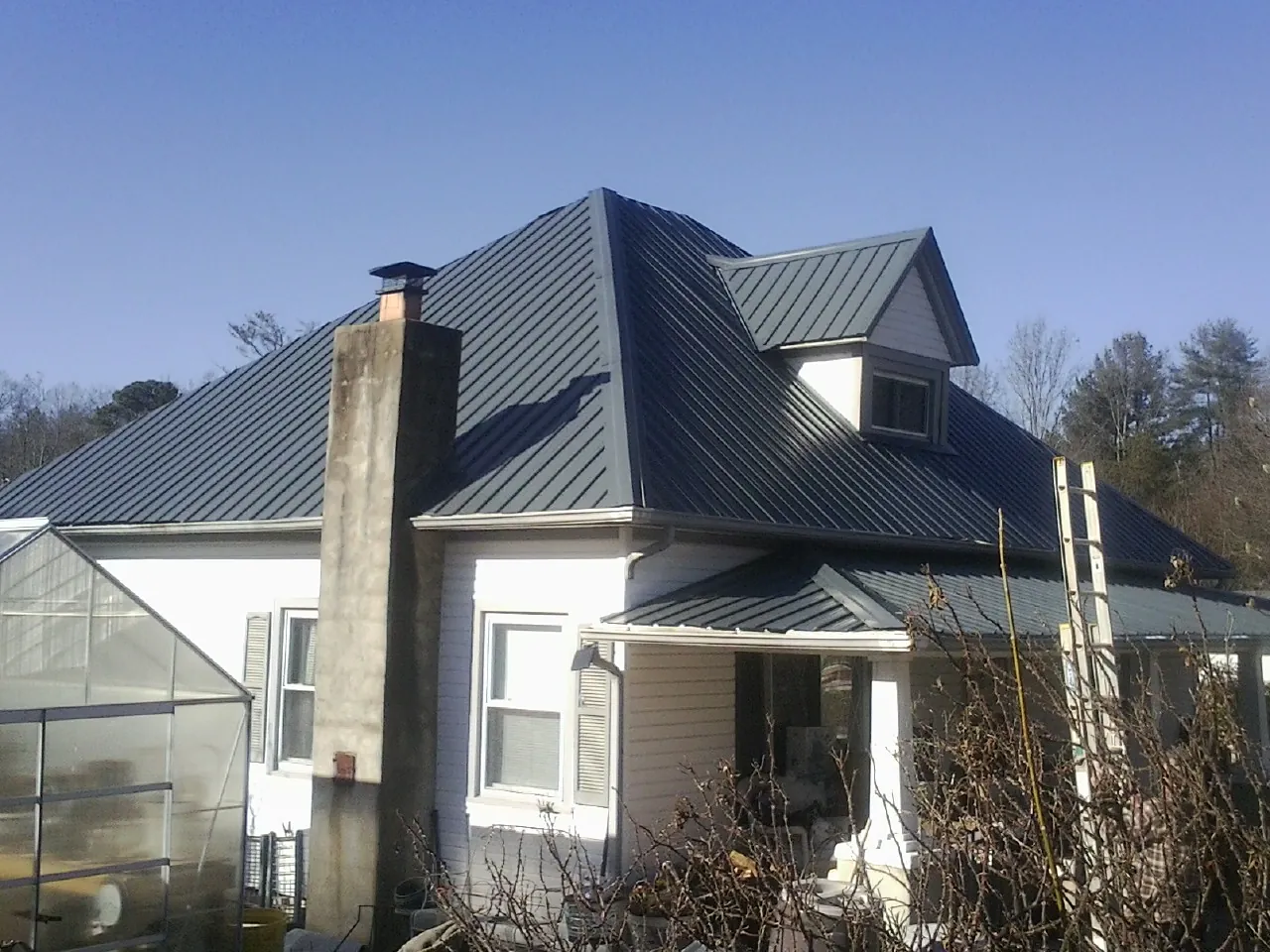 Dark blue standing seam metal roof on a white farmhouse with dormer — Slate & Tile Roof Repair by Roofing Brothers in Grand Forks