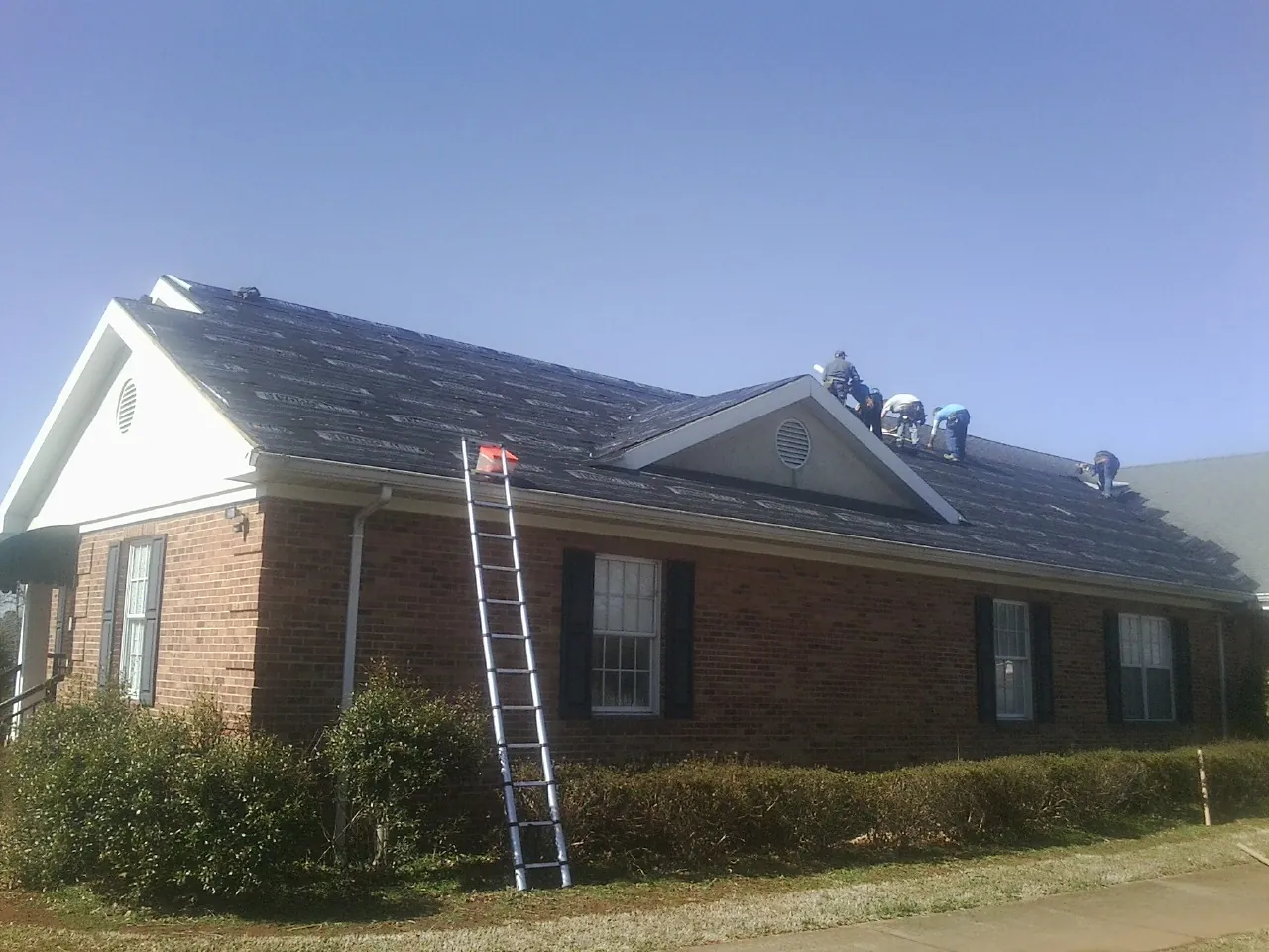 Crew tearing shingles off a brick ranch roof with a ladder set — Emergency Roof Repair work by our crew in Grand Forks