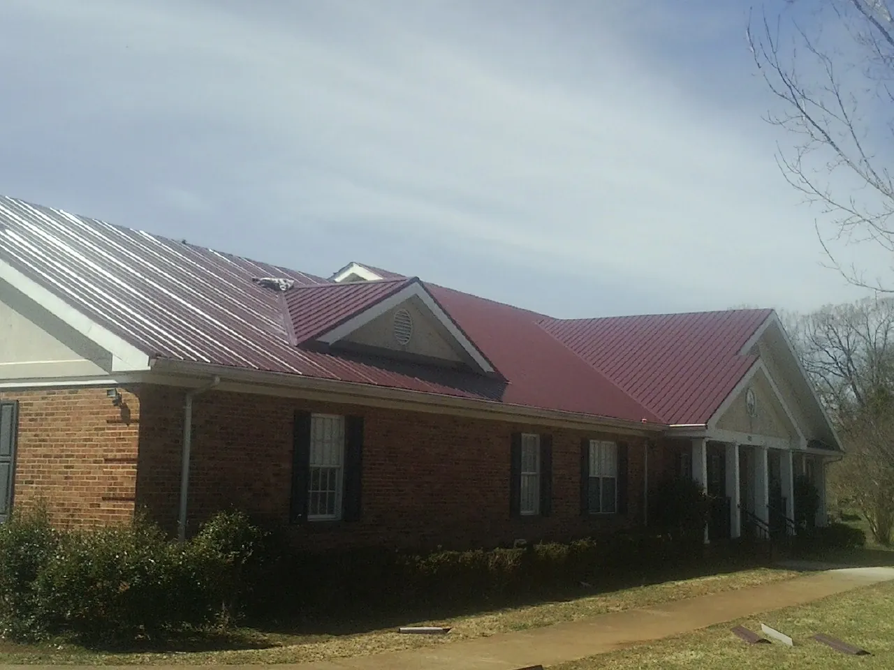 Red metal roof with gabled entries on a long brick building, from a Hail Damage Roof Repair job in Grand Forks