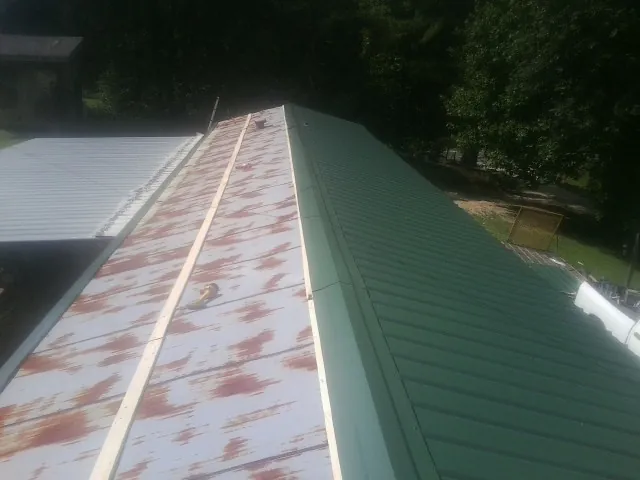 Old rusted panels beside newly installed green metal roofing — Wind Damage Roof Repair by Roofing Brothers in Grand Forks