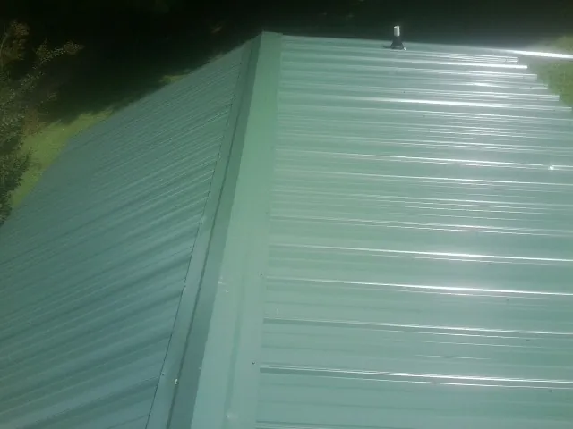 New green metal panels meeting at the ridge of a roof — Flat Roof Repair work by our crew in Grand Forks