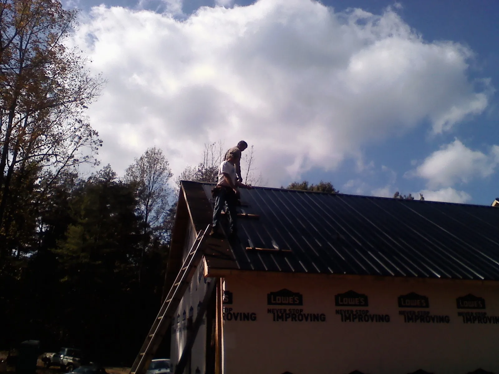Roofer fastening dark metal panels high against a cloudy sky, from a Roof Inspection job in Grand Forks