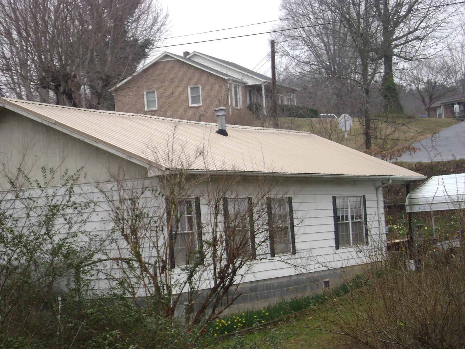 Tan metal roof on a white sided house set into a hillside — Commercial Roofing by Roofing Brothers in Grand Forks
