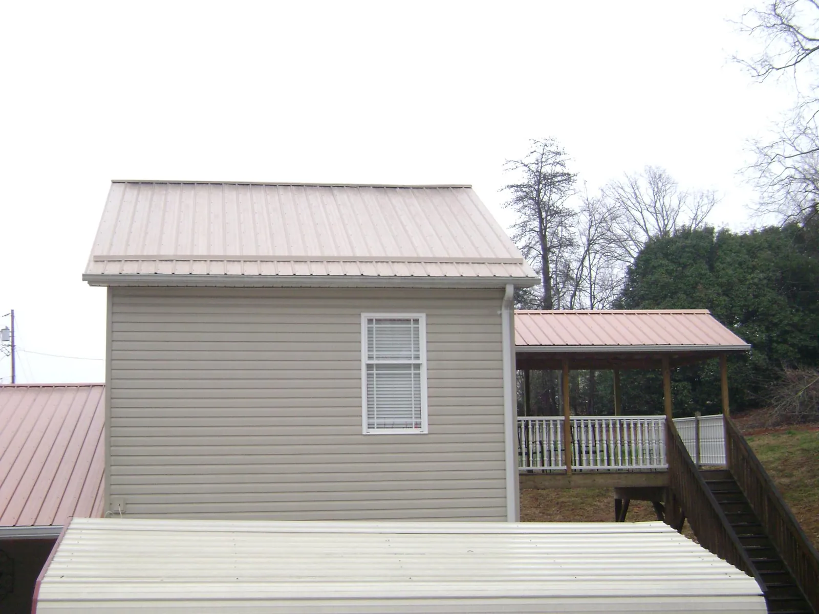 Tan metal roofs on a two story addition and attached porch, from a Roof Replacement job in Grand Forks